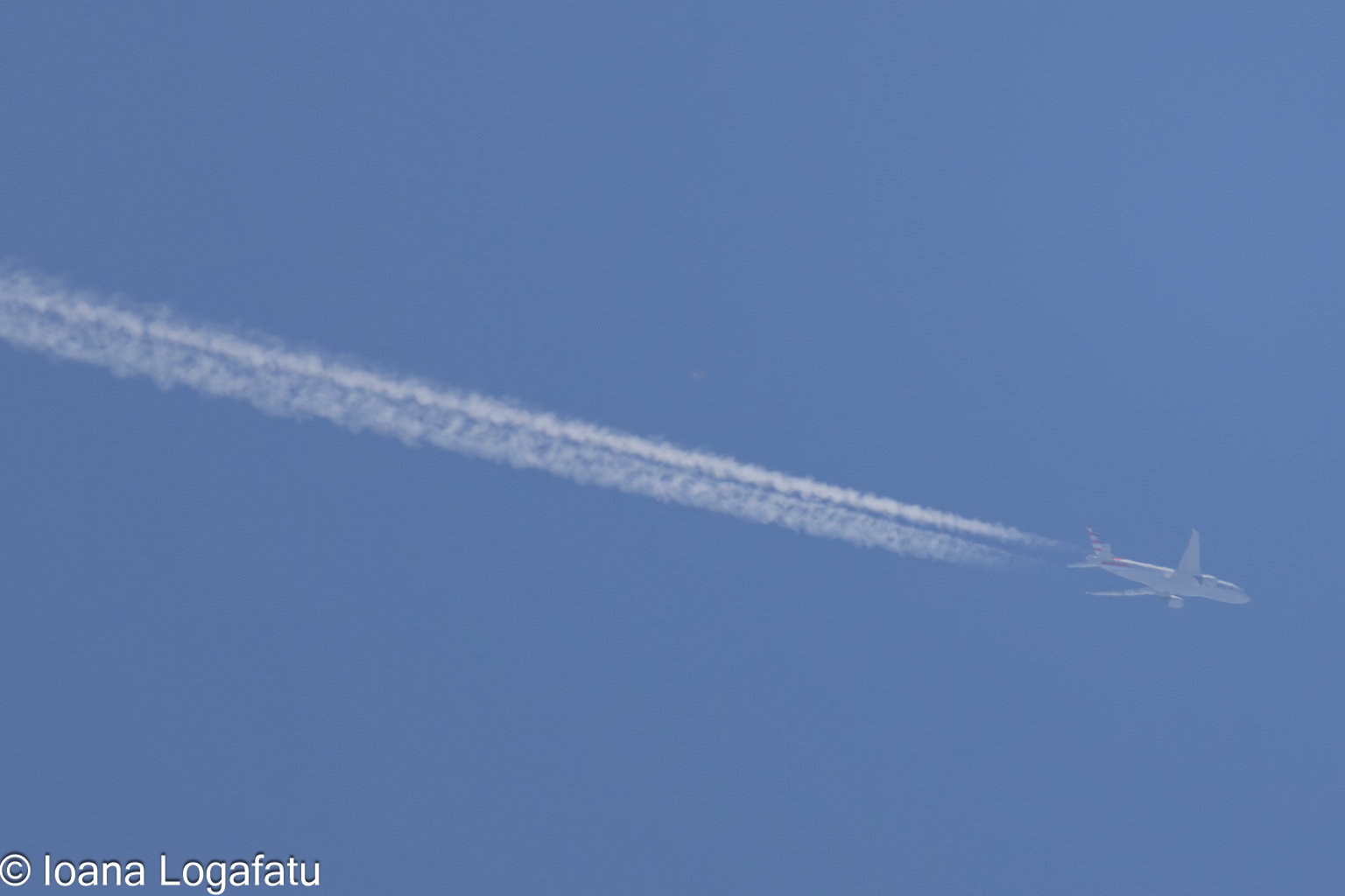 Cloud streaks from soaring airplane over clear sky